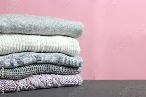 A pile of warm sweaters on a wooden table on a color background. Autumn and winter clothes.