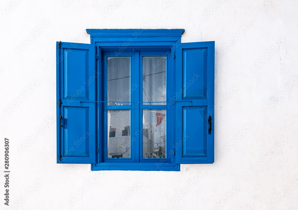 Blue window with open shutters and white wall of greek house in Amorgos, Greece.