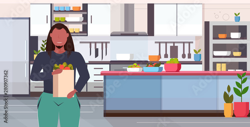 fat overweight man holding groceries shopping bag diet weight loss concept obese guy with vegetables and fruits organic food modern kitchen interior portrait flat horizontal