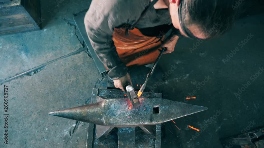 Blacksmith shaping a knife on anvil, hitting it with a hammer. Blacksmith shaping a knife on anvil, hitting it with a hammer.