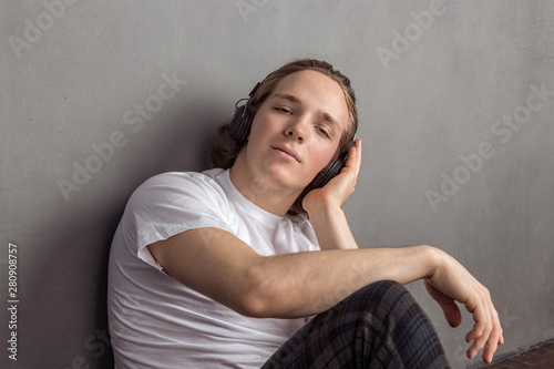 Handsome young man sitting on the floor in living room, having headphones on his head and listening music © Dmitry_Tkachev