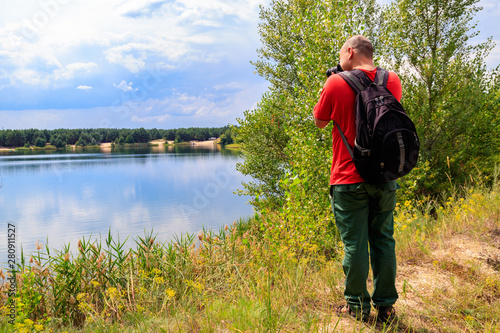 Young traveler man with backpack taking a photos of lake. Travel photography concept