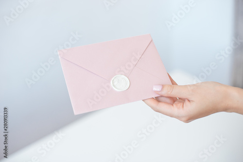 Close-up photo of female hands holding invitation envelope with a wax seal, a gift certificate, a postcard, wedding invitation card.