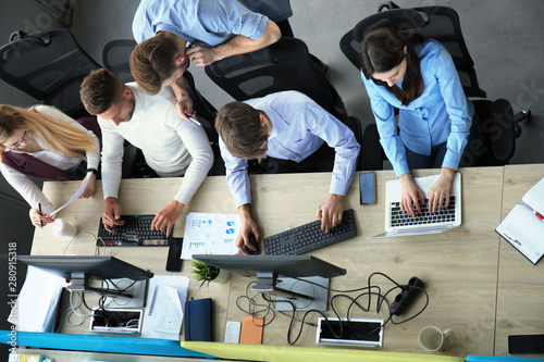 Top view of young modern colleagues in smart casual wear working together while spending time in the office. photo