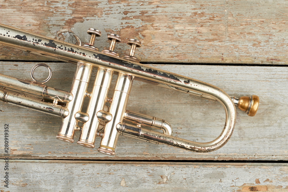 Fototapeta premium Rusty trumpet on wooden surface. Old trumpet on wooden background. Valve of aged trumpet. Antique musical instrument.