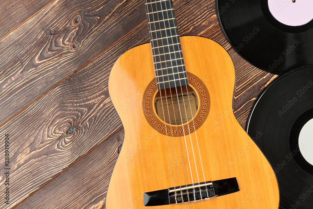 Guitar and vinyl records on wooden background. Guitar, vinyl plates and copy space. Retro music objects.