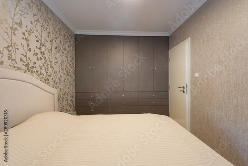 Interior of a beige bedroom with wardrobe wall