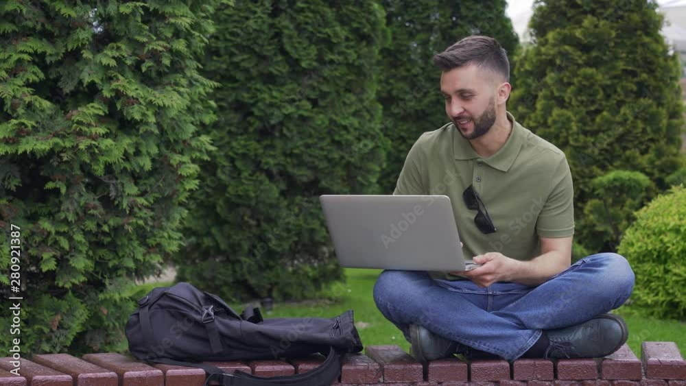 Young man with laptop sitting on a wooden bench in park Young man with laptop sitting on a wooden bench in park