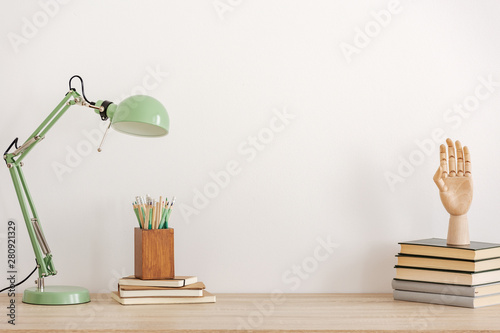 Pastel mint colored lamp on wooden desk with books, copy space on empty white wall photo