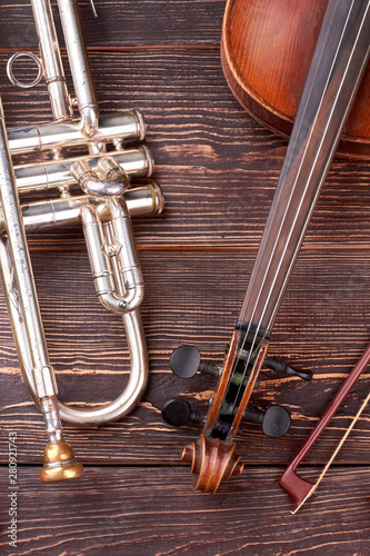 Trumpet and violin on wooden background. Classical musical instruments on brown textured background. Musical equipment in vintage style.