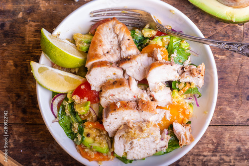 Bowl of salad with quinoa, carrots, avocado, onion, pepper, tomato with lime slices and chopped chicken breast on a rustic wooden background close-up - healthy eating concept