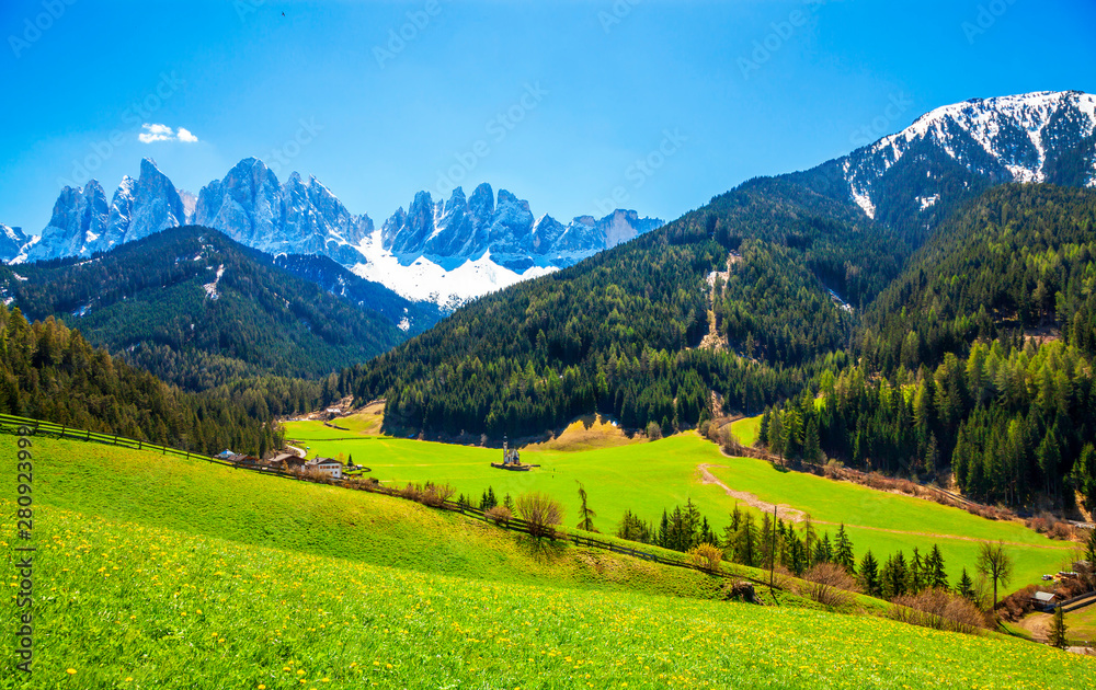 Sunny spring landscape of Dolomite Alps, Italy. Green meadows with dandelions.