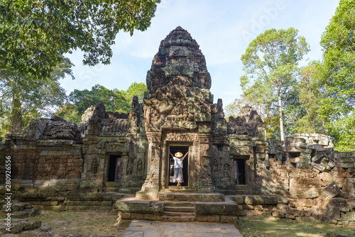 One tourist visiting Angkor ruins amid jungle, Angkor Wat temple complex, travel destination Cambodia. Woman with traditional hat, rear view.