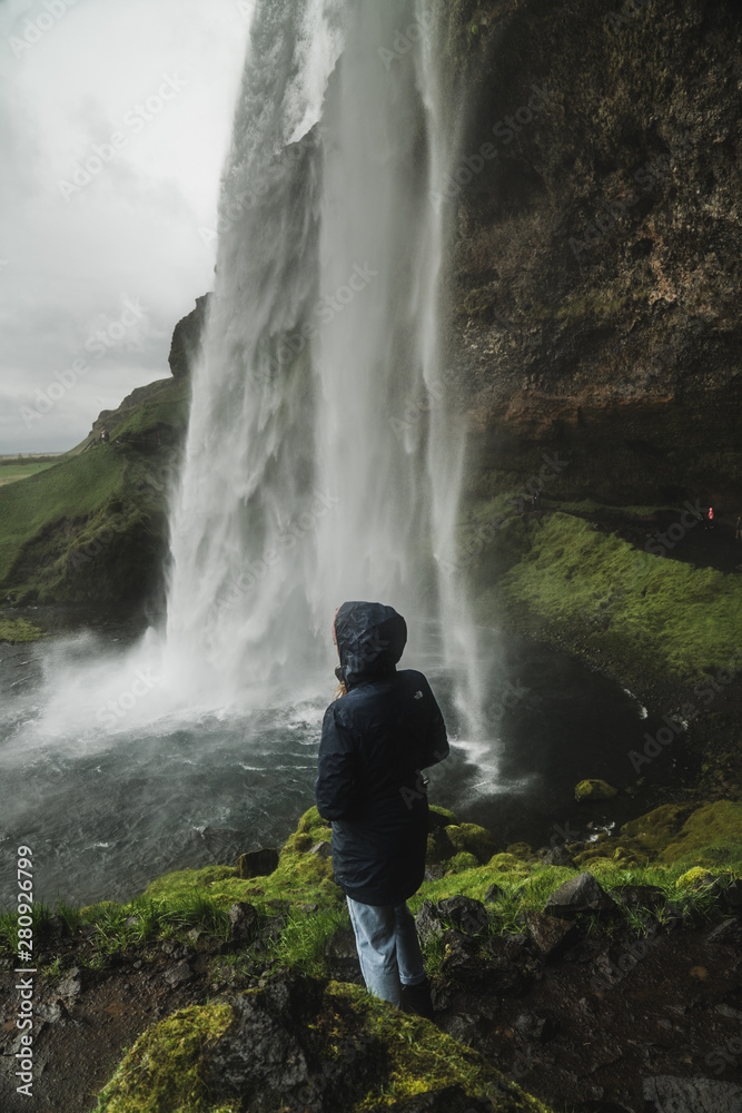 Girl admires beautiful Seljalandsfoss waterfall in Iceland during the spring. 
