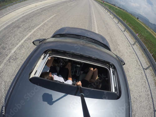 guy with girl driving on the freeway by car and shoot themselves on a selfie stick