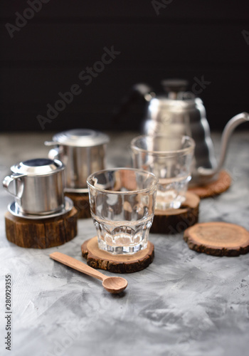 Equipment for making drip coffee Vietnamese style: phin, goose neck kettle and glasses on dark background