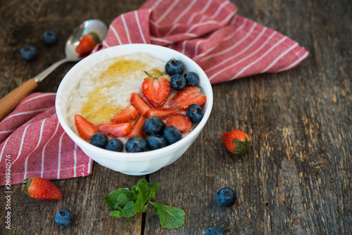 Healthy Breakfast oatmeal bowl with berries and honey on rustic wooden background