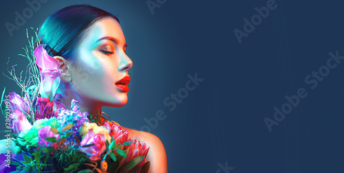 Sexy brunette model girl with bouquet of beautiful flowers. Beauty young woman with bunch of flowers in colorful neon lights. Art design
