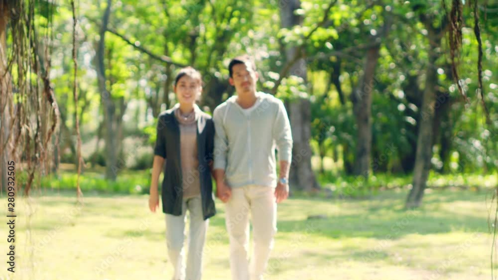asian parents watching two children walking outdoors in park asian parents watching two children walking outdoors in park