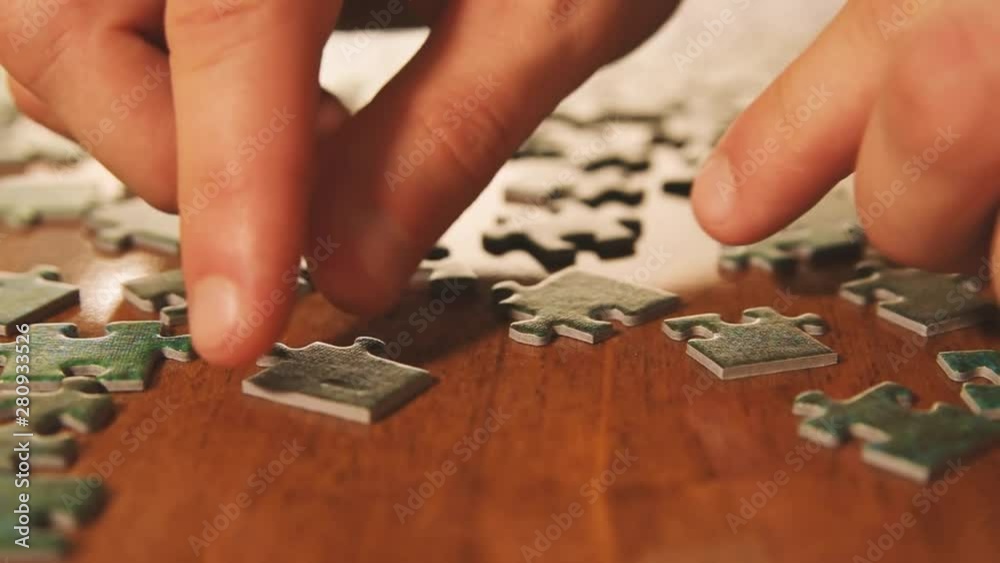 Caucasian male hands assembling jigsaw puzzle pieces. Single pieces and complete puzzle at background. Warm colors