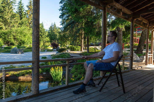 Wallpaper Mural A young man sits on a folding chair on a wooden veranda at dawn and looks ahead Torontodigital.ca
