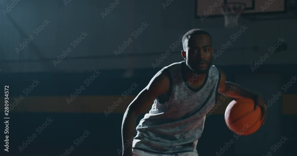 Cinematic slow motion shot of an young african professional male player is practicing a basketball work out in a gym.