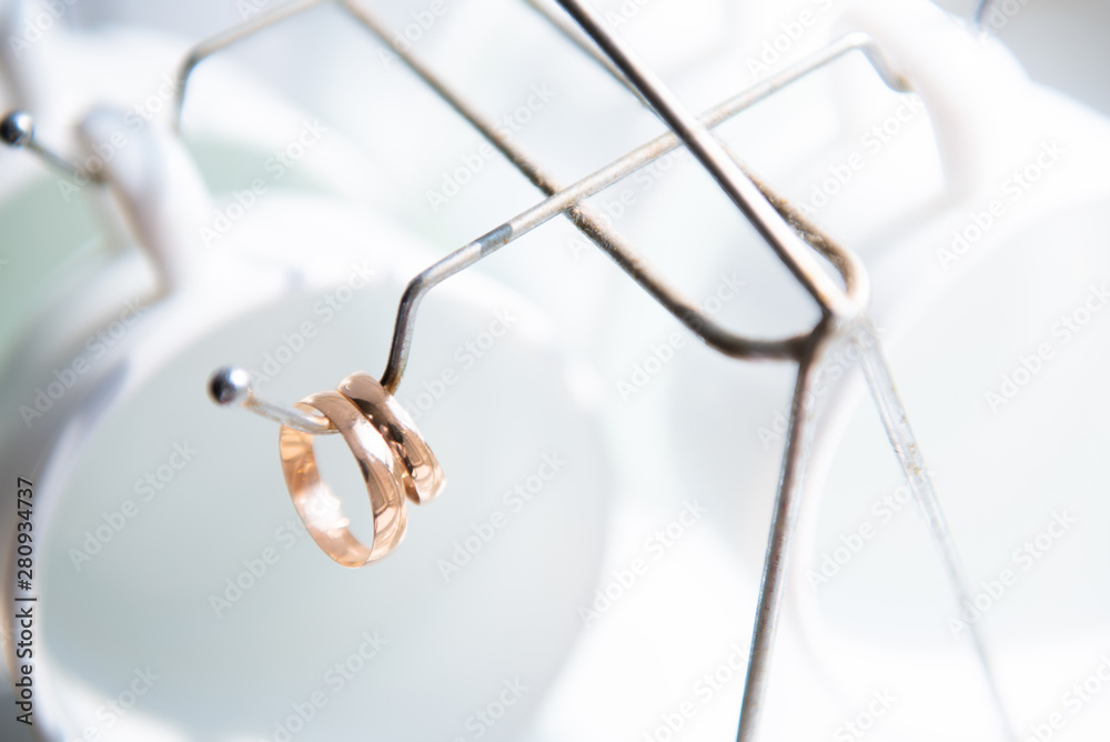 wedding rings and white glasses hanging on the hook from the stand for cups and plates
