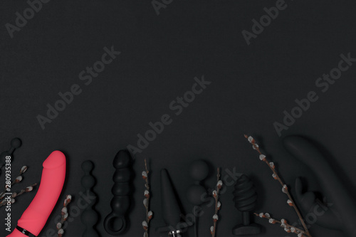 Sex toys. Sex gadgets and masturbation devices. A black dildo, butt plug, anal balls, vibrator and a sprigs of willow on black background. View from above. Place for text. Top view. Sex shop concept