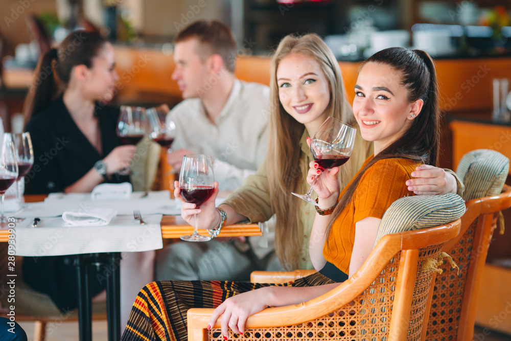Friends have fun drinking wine, talking and smiling in the restaurant. - obrazy, fototapety, plakaty 