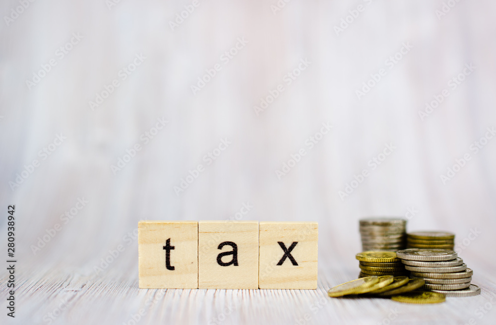 Wooden cube block with word tax and coins on the stack and scattered nearby. Financial management taxes season Wooden cube block with word tax and coins on the stack and scattered nearby. Financial management taxes season