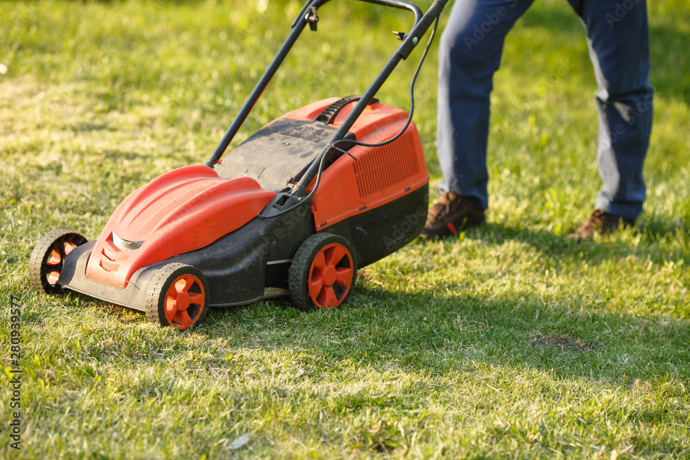 mowing trimmer - worker cutting grass in green yard at sunset. Man with electric lawnmower, lawn mowing. Gardener trimming a garden. mowing trimmer - worker cutting grass in green yard at sunset. Man with electric lawnmower, lawn mowing. Gardener trimming a garden.
