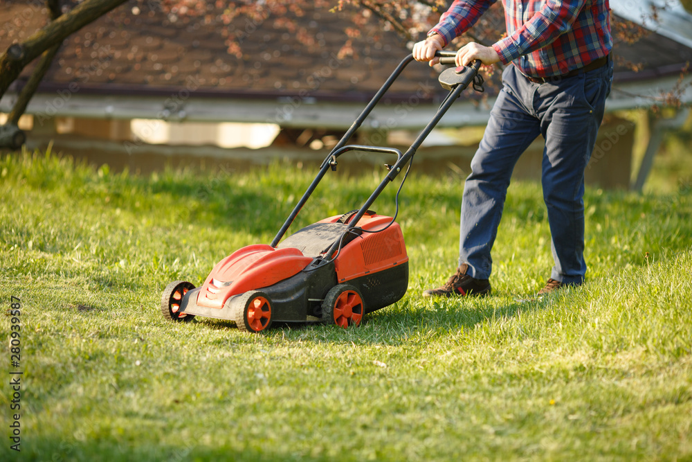 mowing trimmer - worker cutting grass in green yard at sunset. Man with electric lawnmower, lawn mowing. Gardener trimming a garden. mowing trimmer - worker cutting grass in green yard at sunset. Man with electric lawnmower, lawn mowing. Gardener trimming a garden.