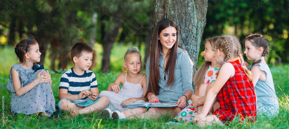 Children and education, young woman at work as educator reading book to boys and girls in park. Children and education, young woman at work as educator reading book to boys and girls in park.
