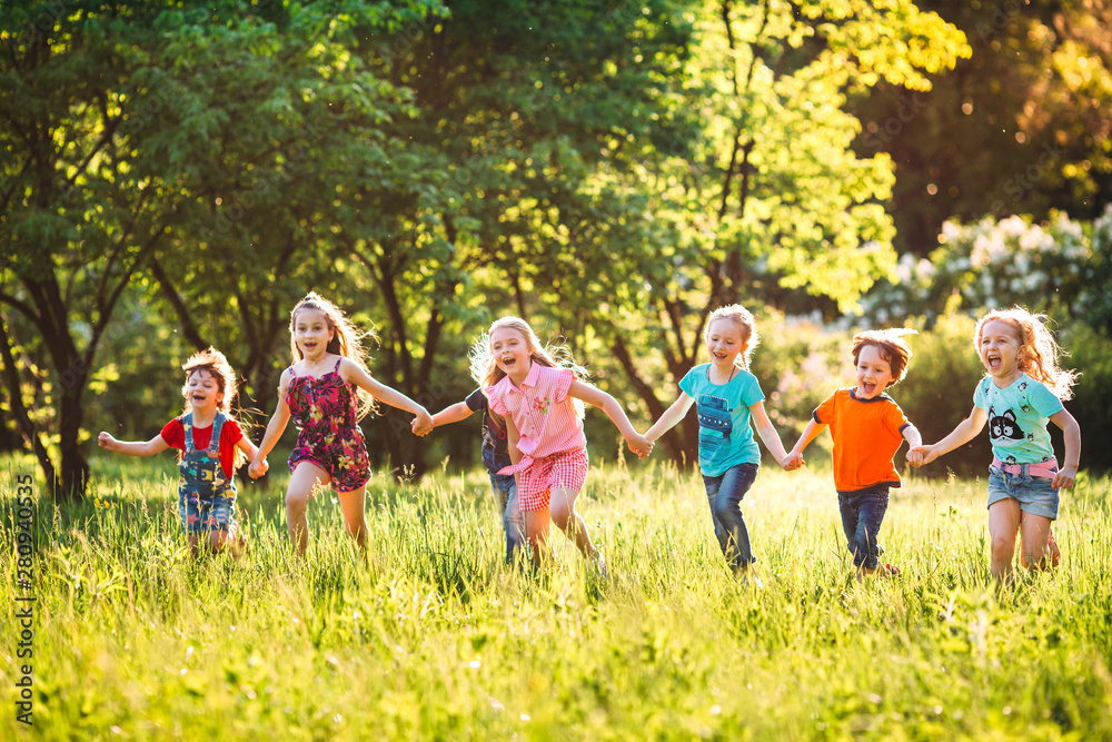 Fototapeta premium Large group of kids, friends boys and girls running in the park on sunny summer day in casual clothes .