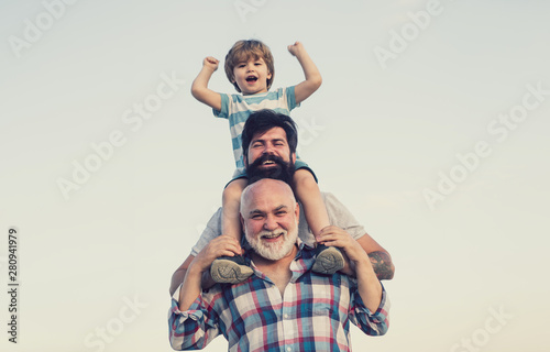 Excited. Father and son playing outdoors. Happy smiling boy on shoulder dad looking at camera. Happy family. Three men generation.