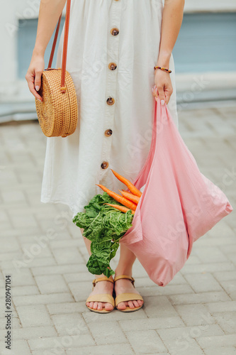 Young woman holding pink cotton grocery bag with vegetables. Reusable eco bag for shopping. Zero waste concept.
