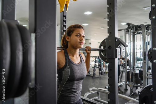 Young beautiful girl in the gym doing exercises on the squat with a barbell, improving the muscles of the buttocks and legs.