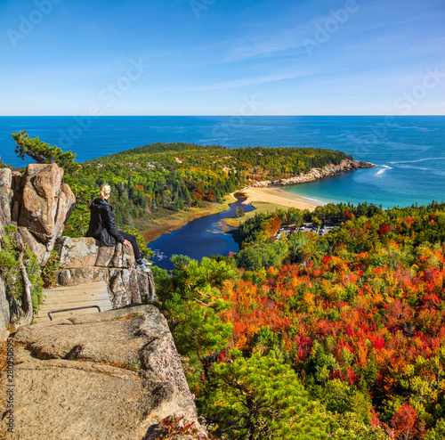 Female hiker sitting on ledge enjoying view of water from Beehive Trail in Acadia National Park