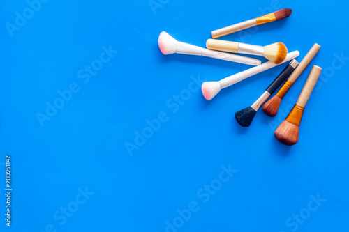 Women desk with brushes for make up on blue background flat lay space for text