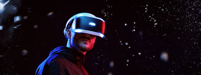 Young man over dark magic light background. Guy in glasses of virtual reality. Augmented reality, game, hobby concept. VR.