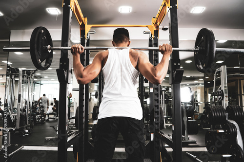 Man at the gym. Execute exercise squatting with weight, in gym