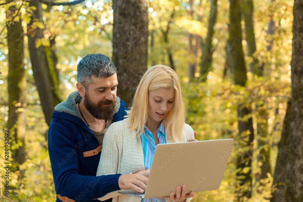 Autumn couple using notebook. Young couple with autumnal mood. Fall concept. Outdoor autumn portrait Gorgeous models with sunny day light. Romantic portrait of a sensual couple in love.