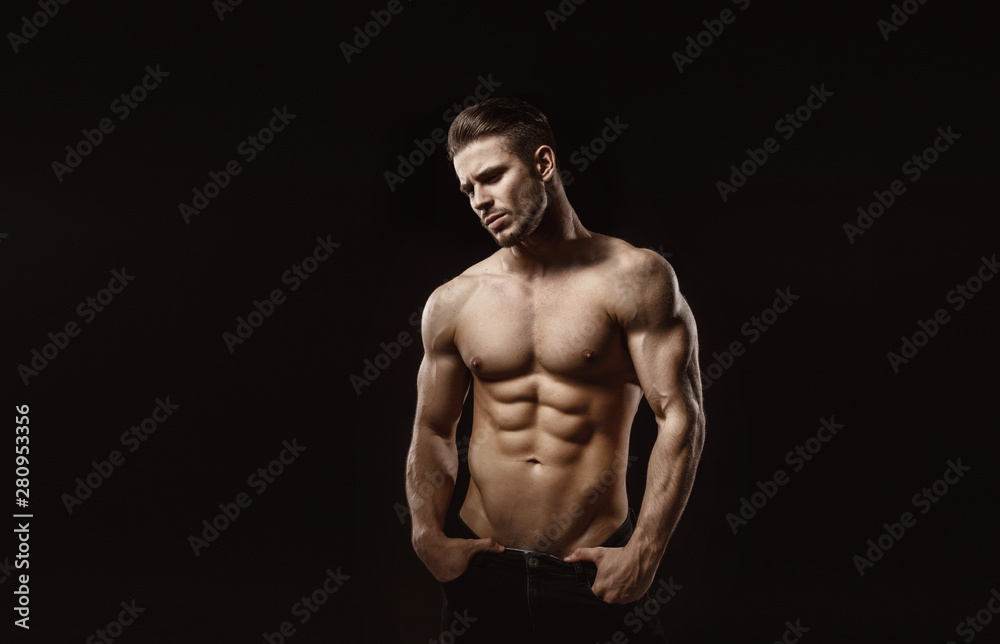 Naklejka premium Muscular model sports young man on dark background. Fashion portrait of strong brutal guy with a modern trendy hairstyle. Sexy torso. Male flexing his muscles.