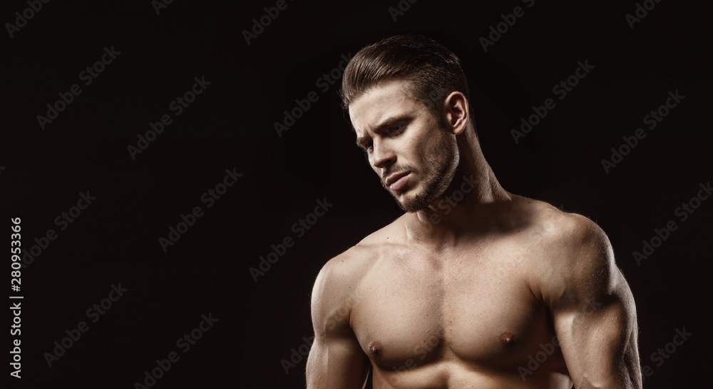 Muscular model sports young man on dark background. Fashion portrait of strong brutal guy with a modern trendy hairstyle. Male flexing his muscles.