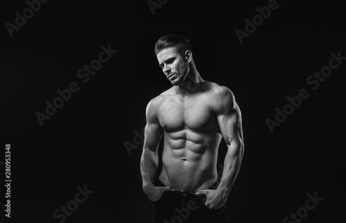 Black and white. Muscular model sports young man on dark background. Fashion portrait of strong brutal guy with a modern trendy hairstyle. Sexy torso. Male flexing his muscles.