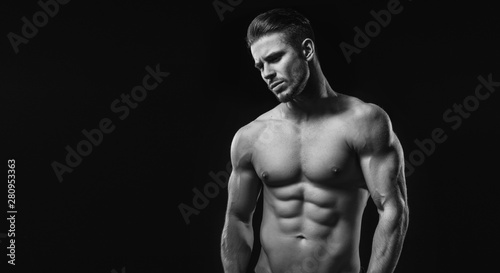 Black and white. Muscular model sports young man on dark background. Fashion portrait of strong brutal guy with a modern trendy hairstyle. Sexy torso. Male flexing his muscles.