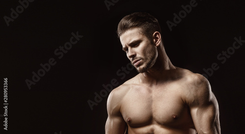 Muscular model sports young man on dark background. Fashion portrait of strong brutal guy with a modern trendy hairstyle. Male flexing his muscles.