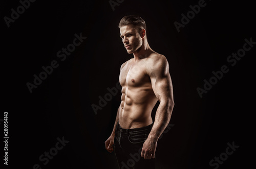 Muscular model sports young man on dark background. Fashion portrait of strong brutal guy with a modern trendy hairstyle. Sexy torso. Male flexing his muscles.