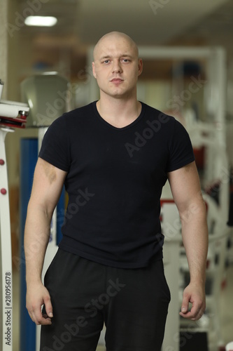 Sporty man in black sportswear. Young guy wearing t-shirt and relaxing in gym. Workout and break concept. Handsome sportsman bodybuilder with an ideal body, after coaching poses in front of the camera