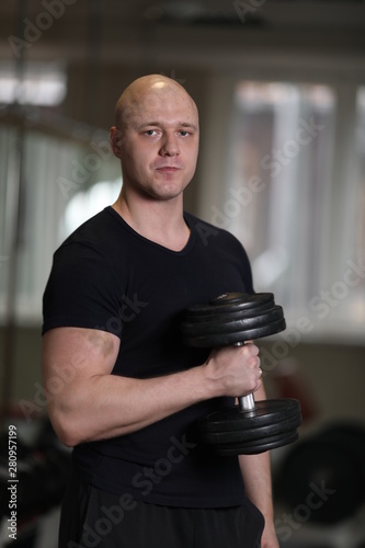 european caucasian athletic man bodybuilder in black sportwear holding dumbell and showing his muscular arms. man doing exercise for biceps. Background is gym